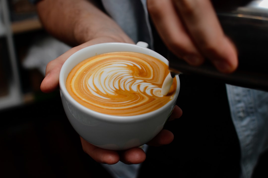 A collection of essential tools for creating latte art, including a milk frother, steaming pitcher, and latte art pen, arranged on a wooden countertop with a cup of coffee in the background.