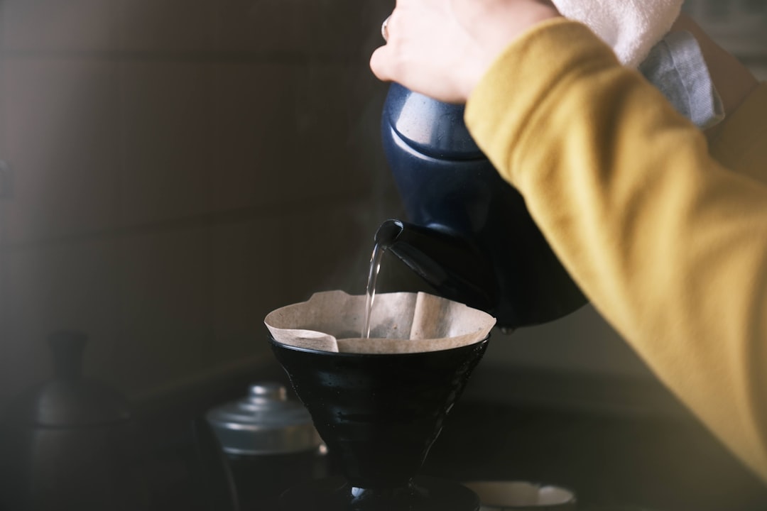 A close-up of a manual coffee brewing setup with a pour-over dripper, freshly ground coffee, and a kettle.